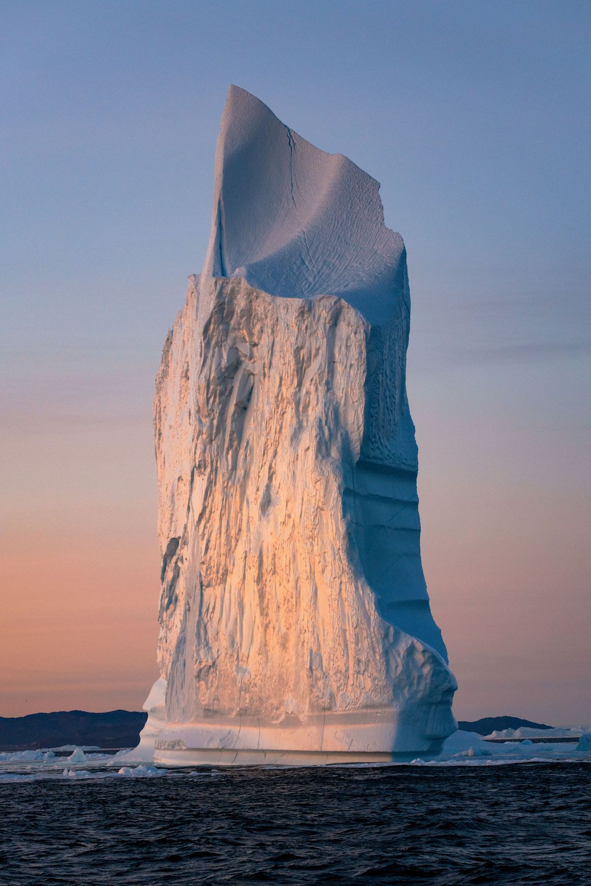 Puesta de sol detrás de una torre de hielo en la bahía de Disko