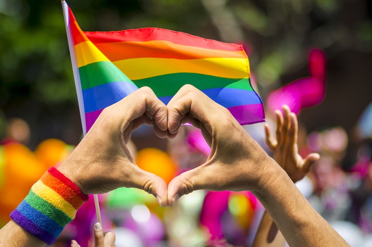 Heart Sign Formed with Hands with Gay Pride Flags in the Background