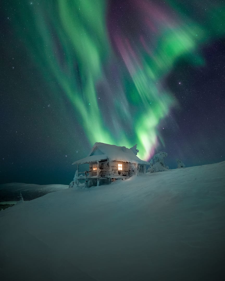 Cabaña nevada en Finlandia con la aurora boreal de fondo