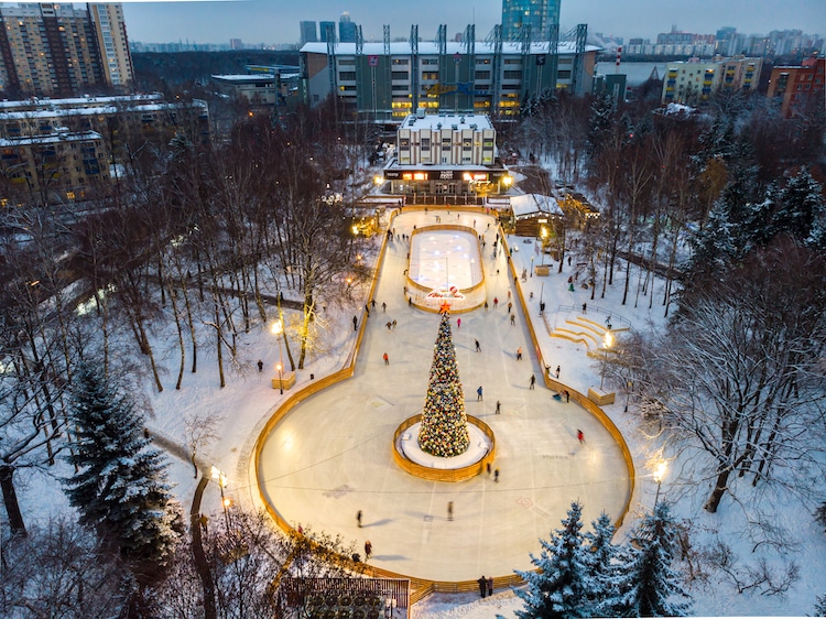 Aerial view of people skating on an outdoor ice rink with a Christmas tree installed.