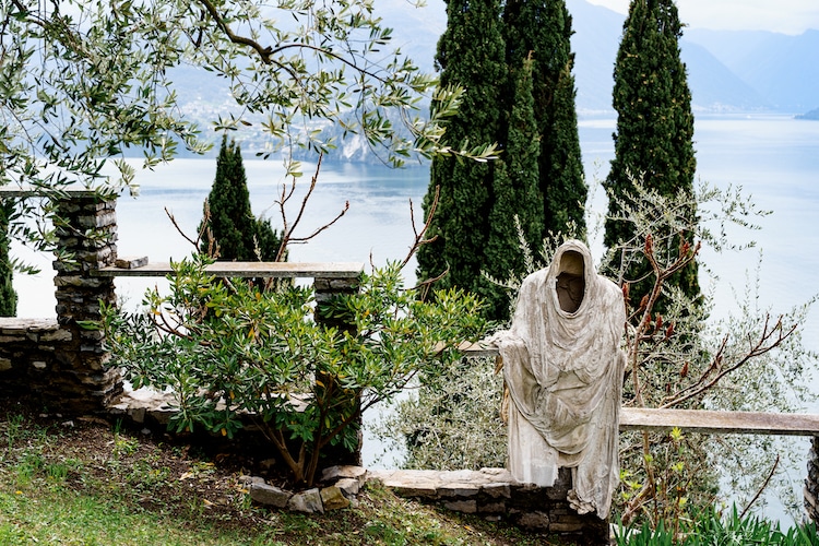 Ghost statue on a stone fence among green trees on the shores of Lake Como. Italy