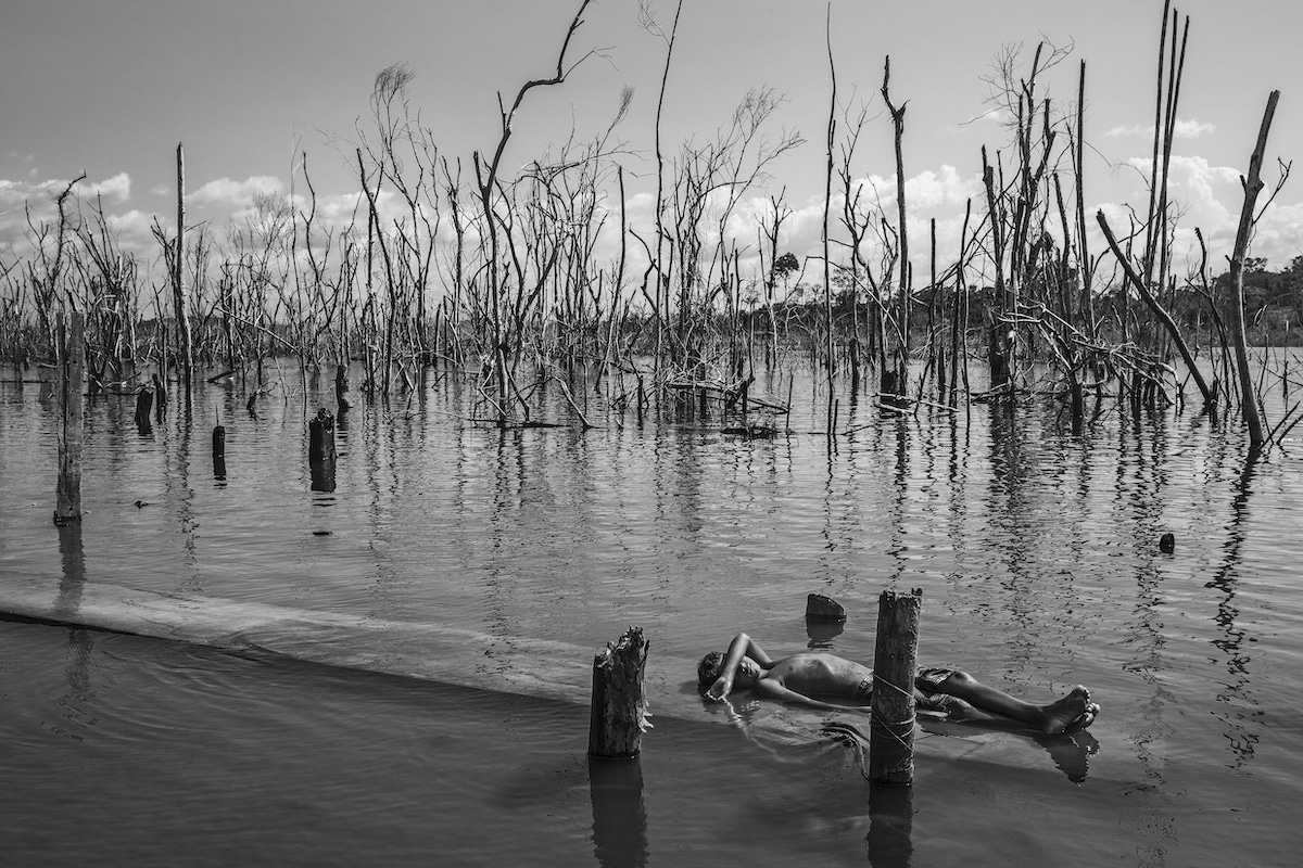 Boy rests on a dead tree trunk in the Xingu River in Paratizão