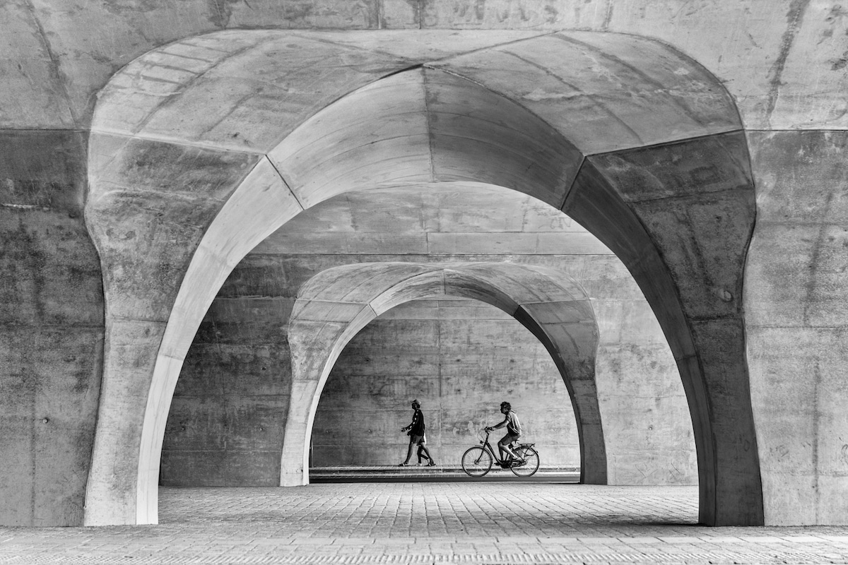 아치 아래에서 걷고 자전거를 타는 사람들의 흑백 사진