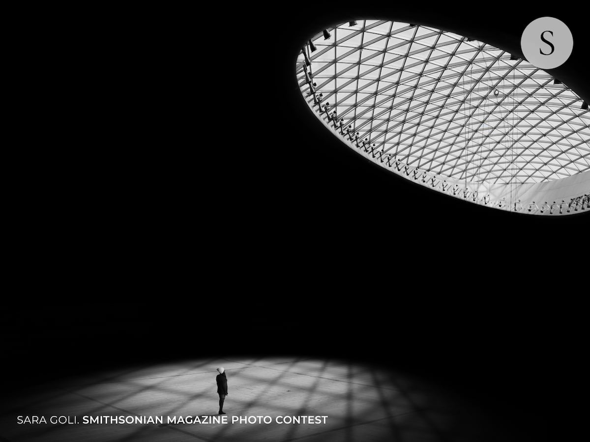 Black and White Photo of a Person Standing Under a Skylight