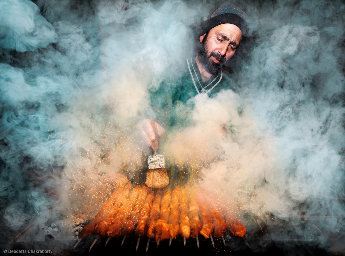 Hombre rodeado de humo mientras hace kebabs en la India