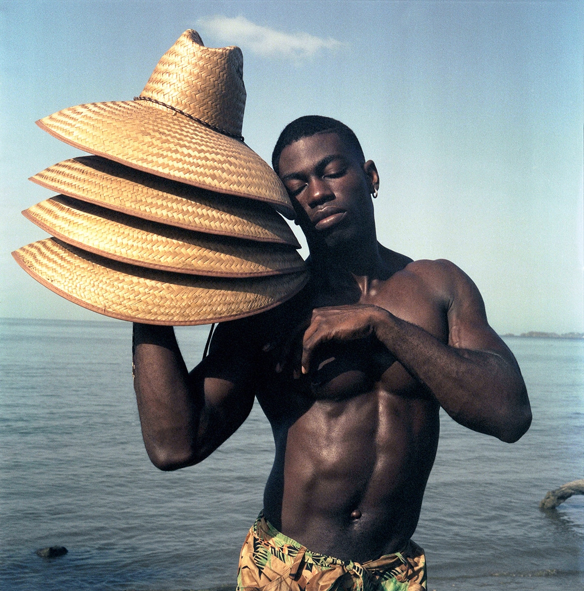 Black Man at the Beach Holding Straw Hats