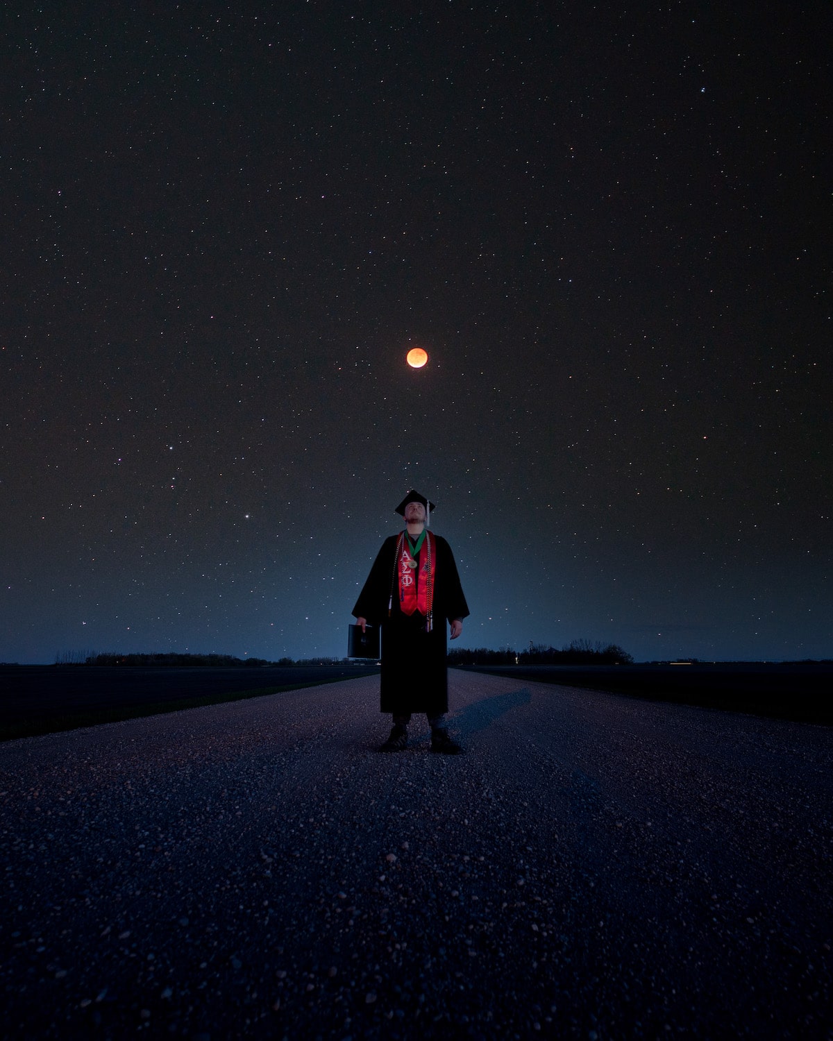Unique Graduation Photo of a Grad Standing Under Lunar Eclipse