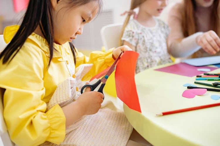 Little girl in a yellow dress cutting colored paper