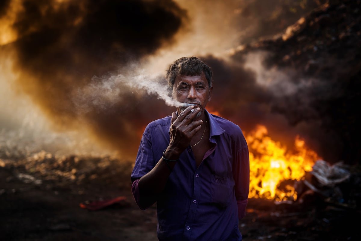Man Smoking Cigarette by Burning Garbage in Bangladesh