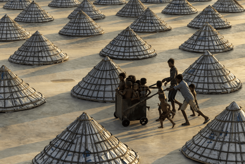 Children weave in and out of scores of giant cones at a rice processing plant in Bangladesh