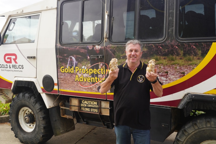 Man poses in front of a truck holding two halves of the largest gold nugget found in australia