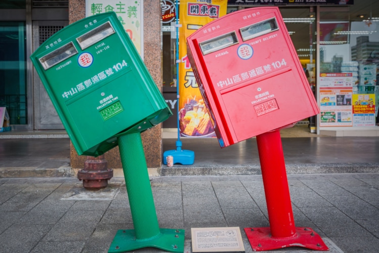 two taiwanese mailboxes bent by a hurricane, one green and one red