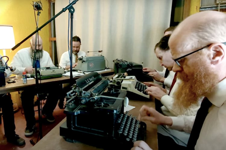 A group of men type on vintage typewriters to make music