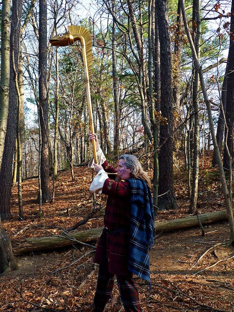 Golden Celtic Carnyx being played by a man in a forest