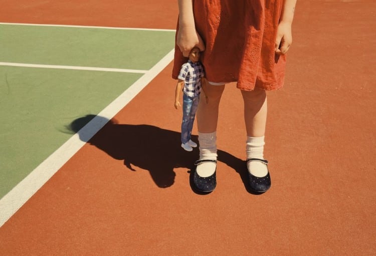 Little Girl Holding a Doll on a Tennis Court