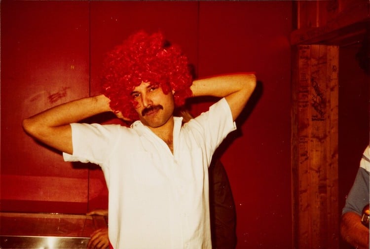 Freddie Mercury posing with a bright red curly hair wig