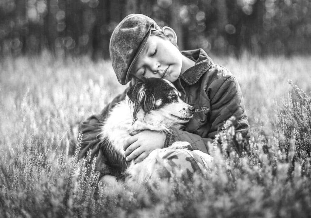 Young boy hugging his dog while sitting in a field