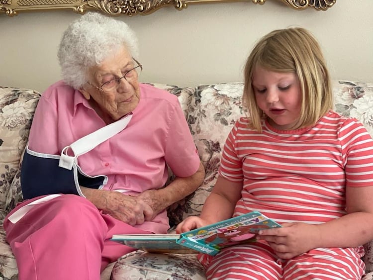 Girl reads aloud from book to senior woman