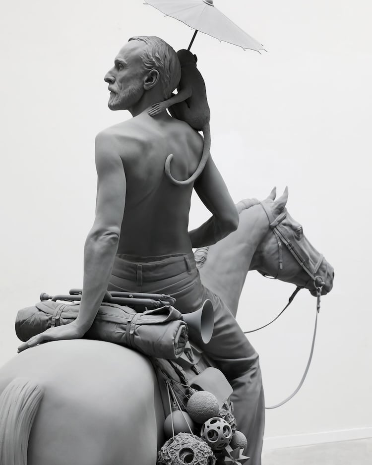 Figurative sculpture of a man on horseback with a monkey holding a parasol on his shoulder in gray monochrome by Hans Op De Beeck