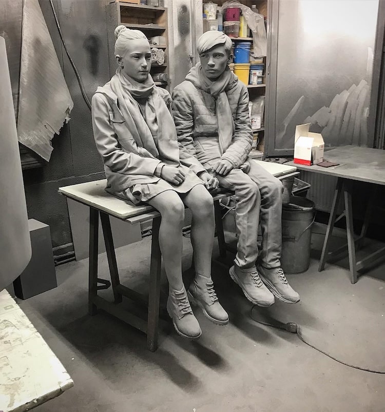 Figurative sculptures of two youths sitting beside one another in gray monochrome by Hans Op De Beeck
