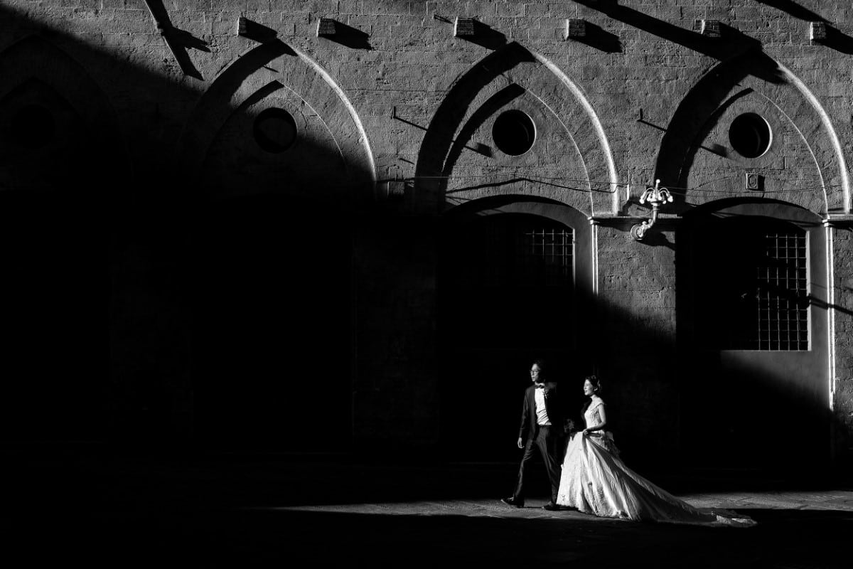 Black and white white photo of bride and groom against Palazzo del Rettorato in Siena