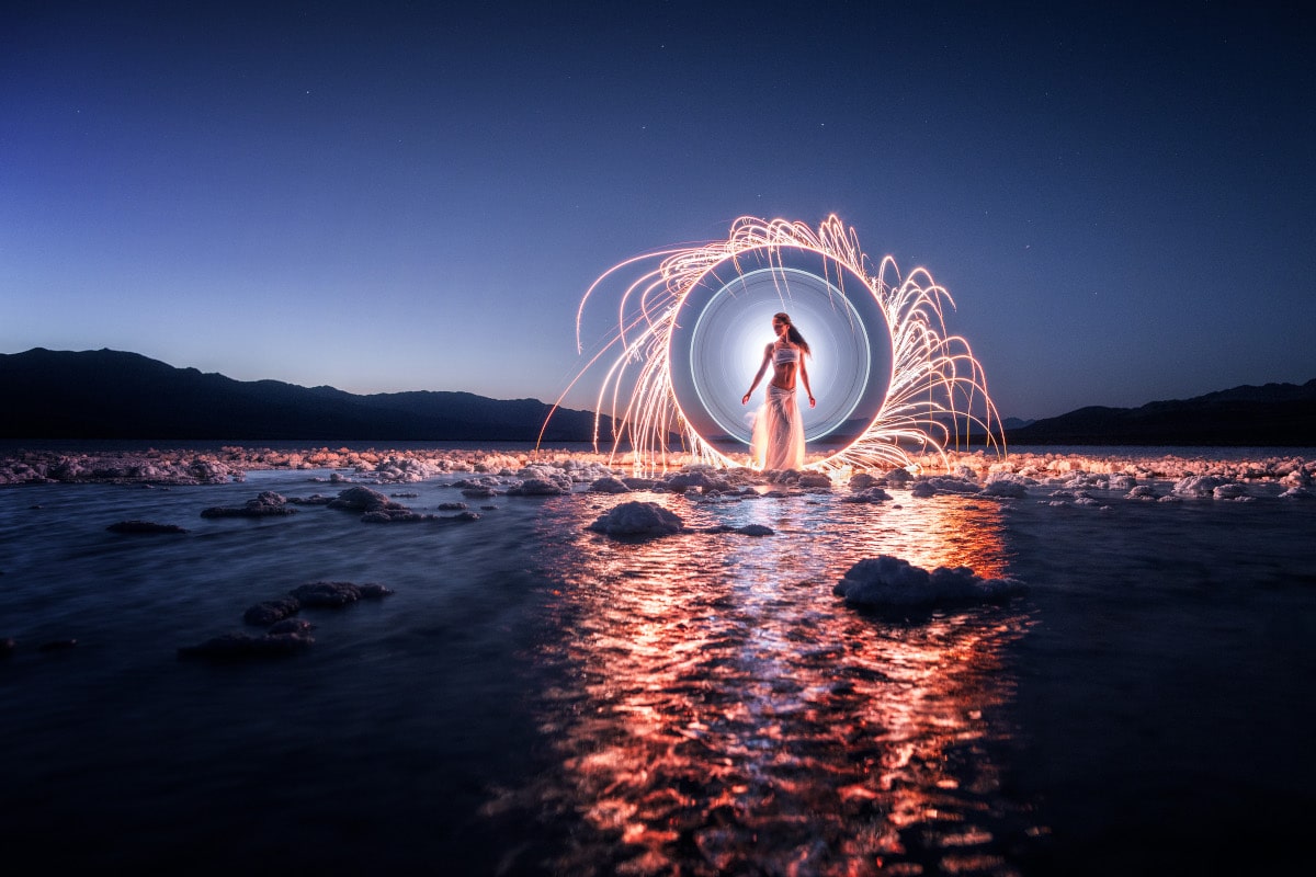 woman stands in front of light halo with water reflections in the foreground