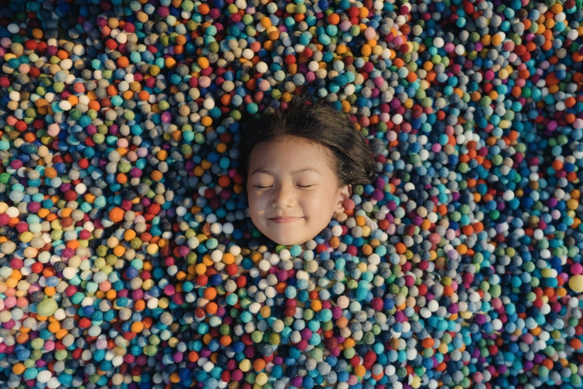 Girl envolped in a pool of felt balls