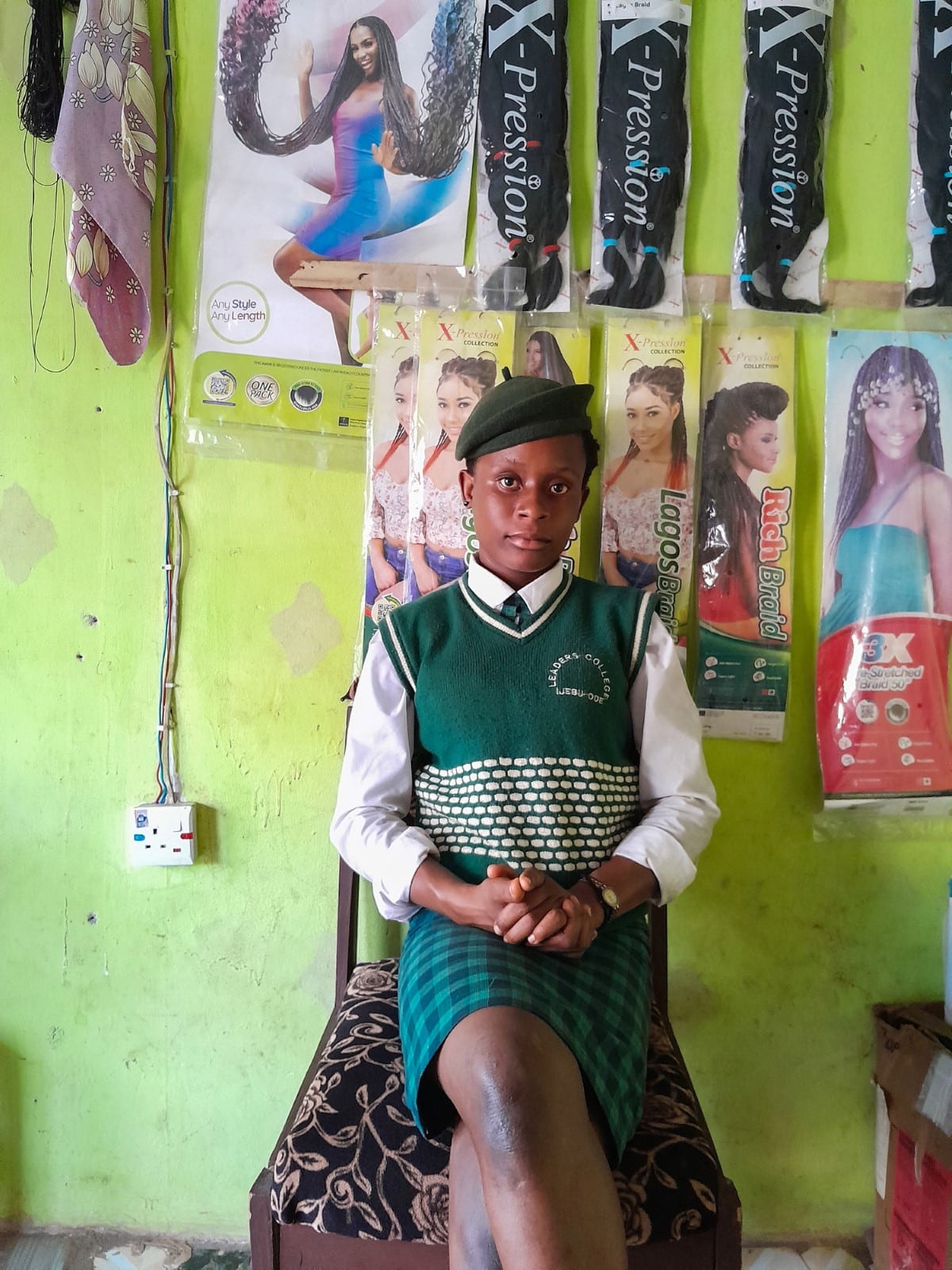 Nigerian girl in a school uniform posed against the wall of a salon