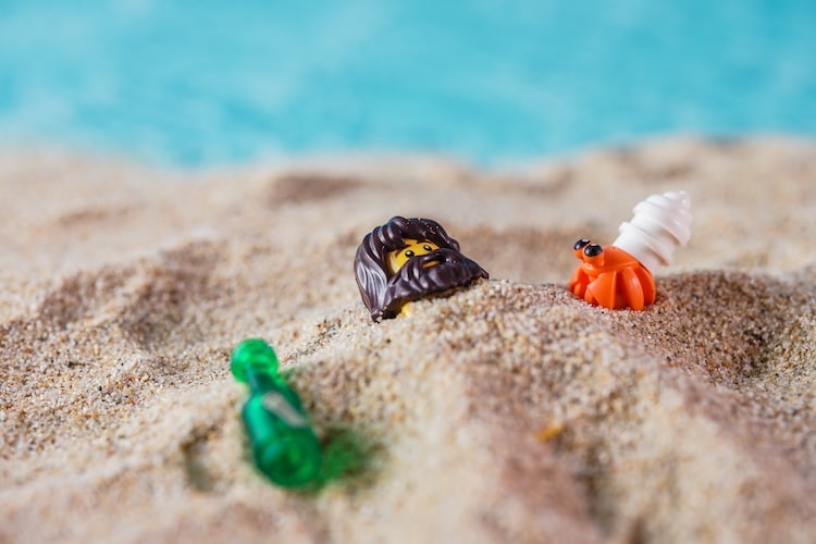 Lego minifigure man with a bear buried in sand