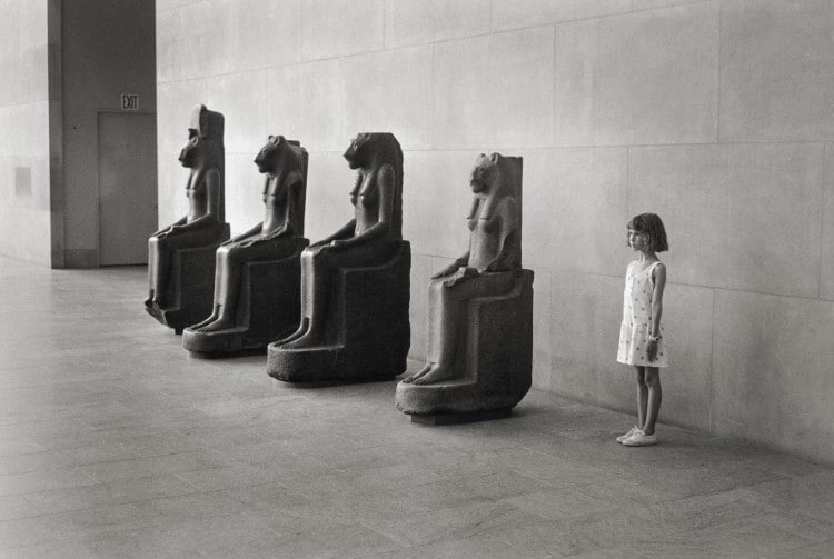 Girl posing next to Egyptian statues at the Metropolitan Museum of Art by Elliott Erwitt