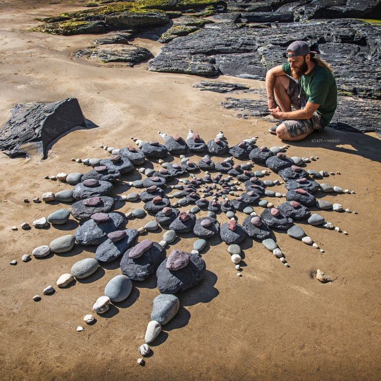 Jon Foreman Sits By An Arranged Spiral of Rocks On Beach