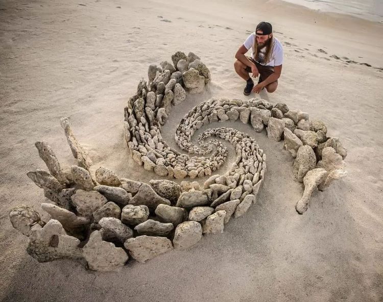 Jon Foreman Kneels Next To Spiral Made Of Rocks On Beach