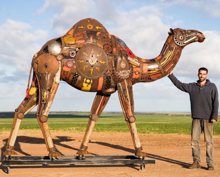 Jordan Sprigg Stands Next To His Metal Camel Sculpture