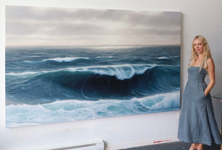 Artist Katharine Burns poses in front of ocean painting