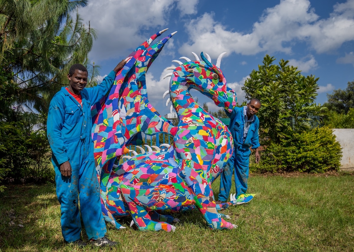 Two men standing next to a dragon made of discarded and upcycled flip-flops