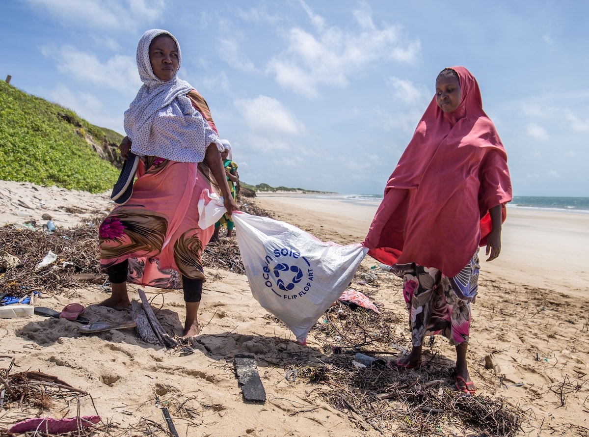 Two women walking on a beach holding an Ocean Sole bag filled with beach waste