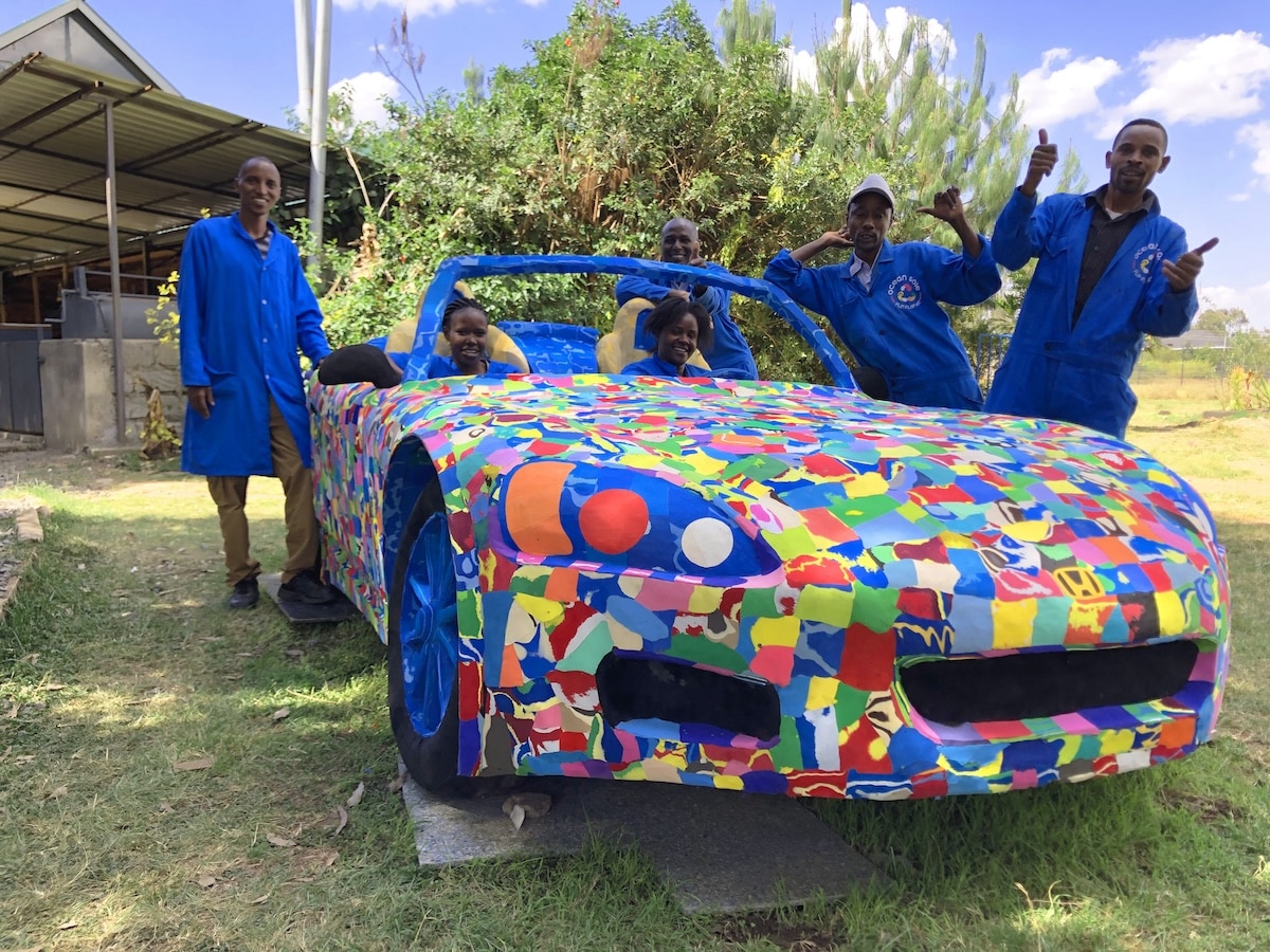 A group of people standing around and sitting in a life-size convertible car made of colorful flip-flops