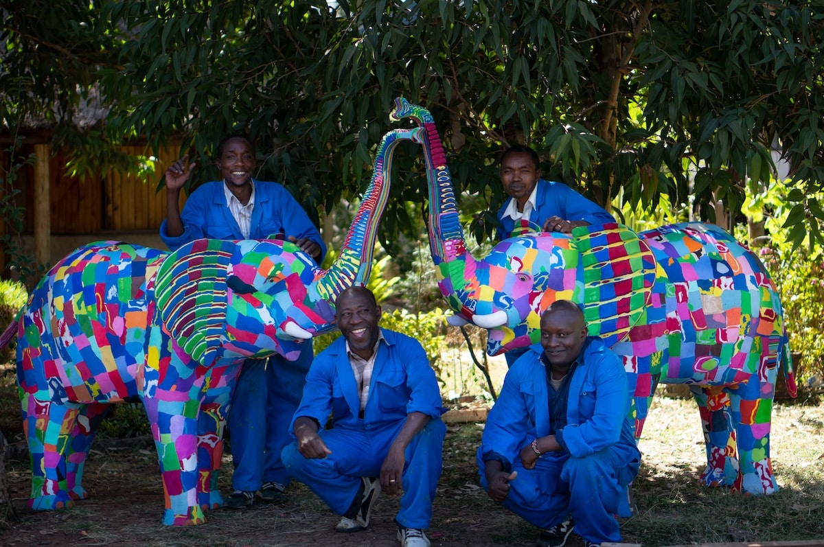 A group of men standing around two elephant sculptures made of colorful flip-flops