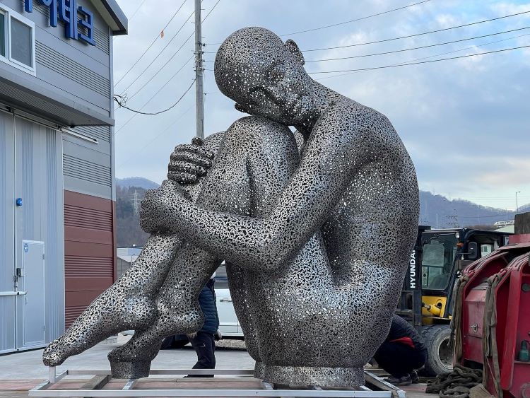 A Sculpture Of A Person In The Fetal Position Made Of Bicycle Chains