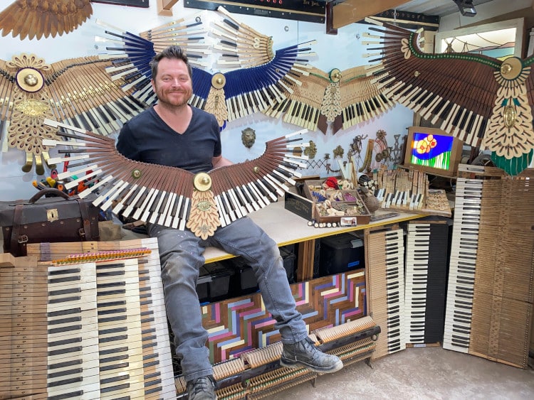David Cox posing with his phoenix sculptures made out of old pianos