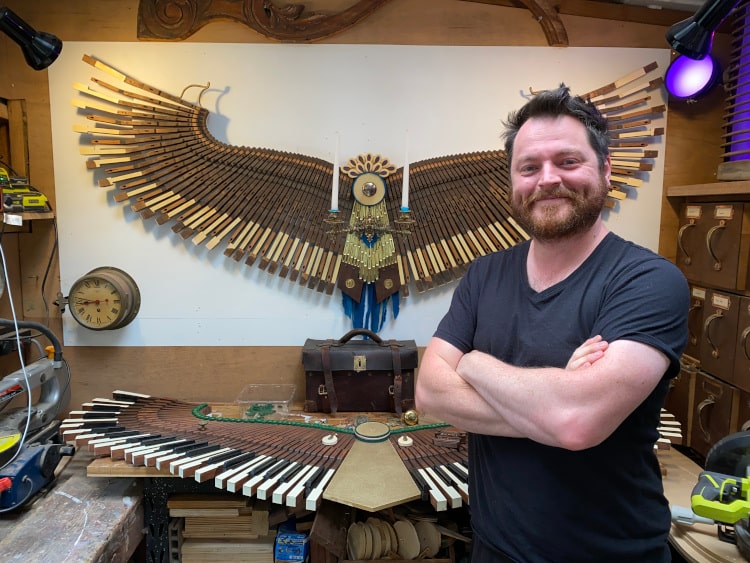 David Cox posing with his phoenix sculptures made out of old pianos