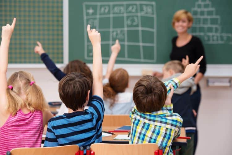 Photo Of Young Children In Classroom With Raised Hands
