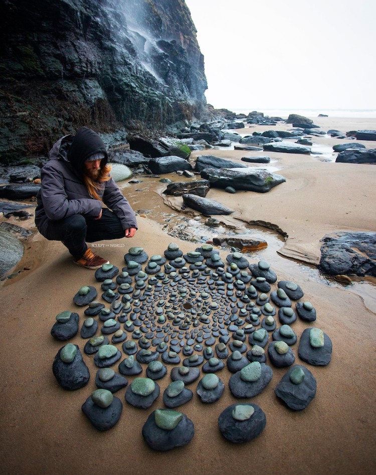Jon Foreman's installation titled Discio 2024, includes an arrangement of stones ini a circular pattern on a sandy beach. Jon Foreman is included in this image, as he gazes over his work. 