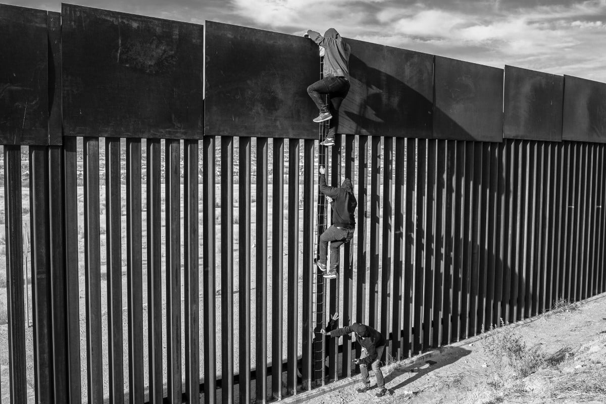 Migrants use a homemade ladder to climb a section of the border wall with the help of a smuggler. 