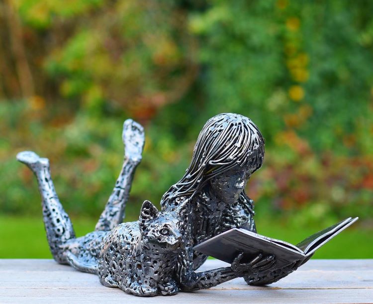 Sculpture Of Little Girl Reading Book Accompanied By Cat Made Out Of Scrap Metal