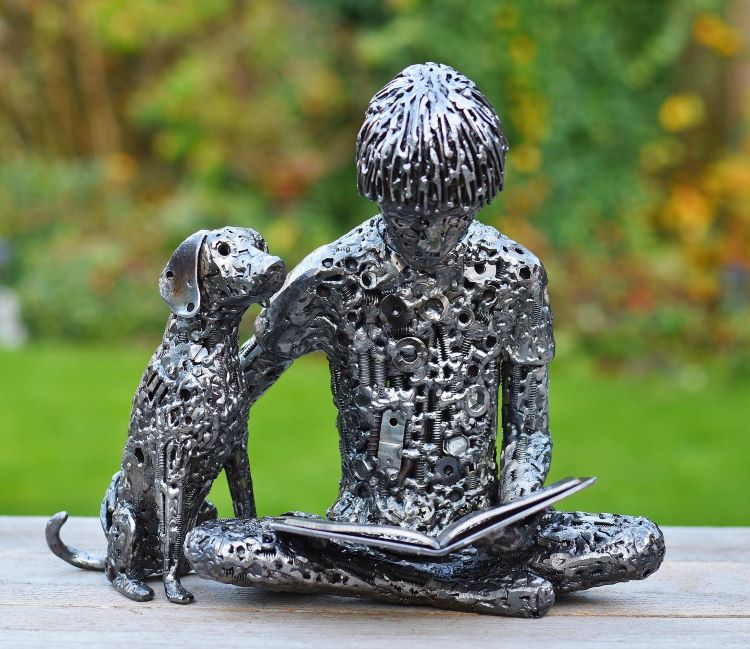 Sculpture Of Little Boy Reading Book Accompanied By Dog Made Out Of Scrap Metal