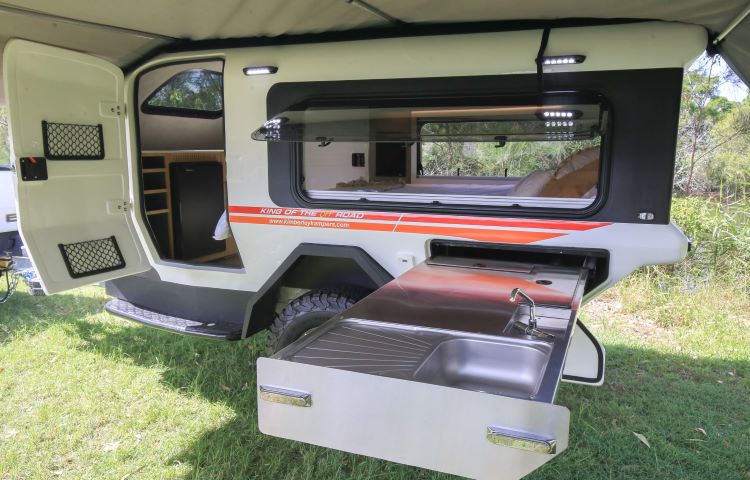 Photo From The Outside Of A Camper Showing The Inside Bed And Pull Out Kitchen