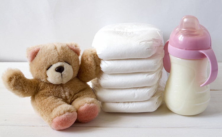 New born child stack of diapers, tebby bear toy on a white wooden background