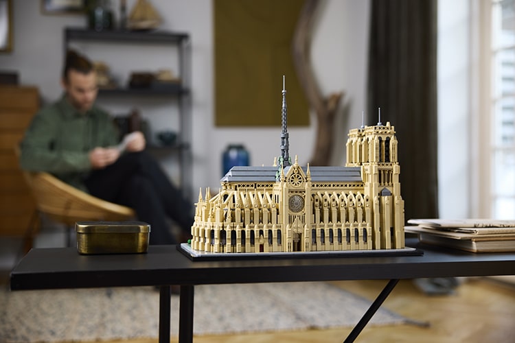 The complete model from LEGO's Architecture Notre-Dame Cathedral is sitting on a coffee table with a man reading in the background.