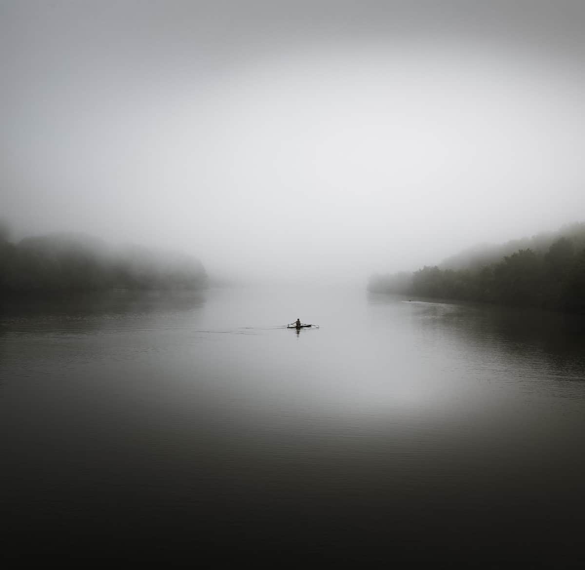 호수 한가운데에서 보트를 저어가는 사람의 흑백 사진